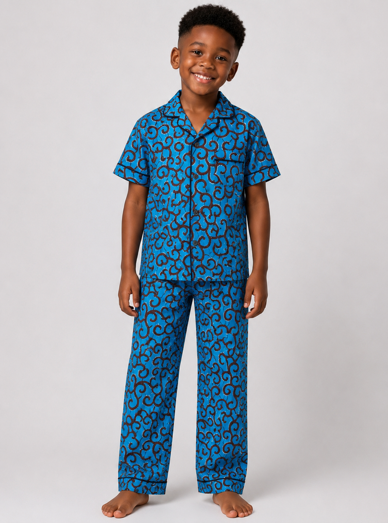 A young boy wearing a two-piece pajama set with a blue and black abstract pattern, standing against a light gray studio background.